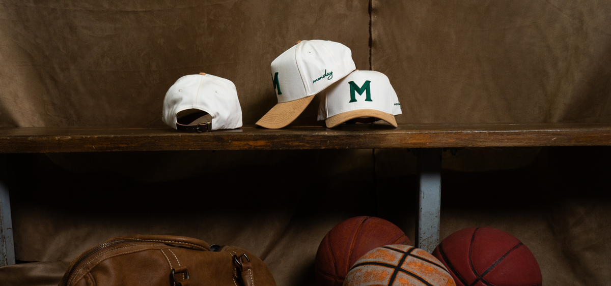 Three caps on a wooden shelf with basketballs below, against a brown background