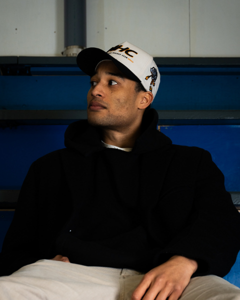 Man wearing a cap sitting on bleachers with a blue background